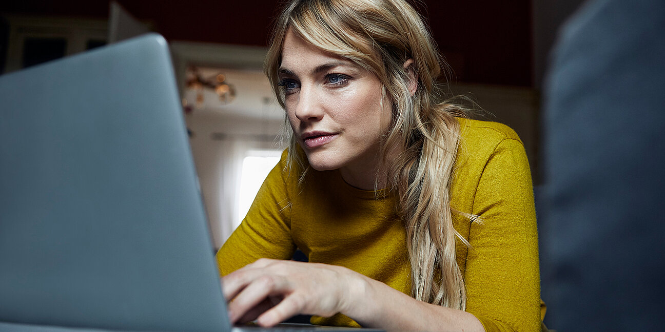 Porträt einer Frau, die zu Hause auf der Couch liegt und einen Laptop benutzt