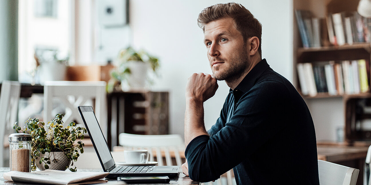 Mittlerer erwachsener Mann, der wegschaut, während er am Laptop sitzt